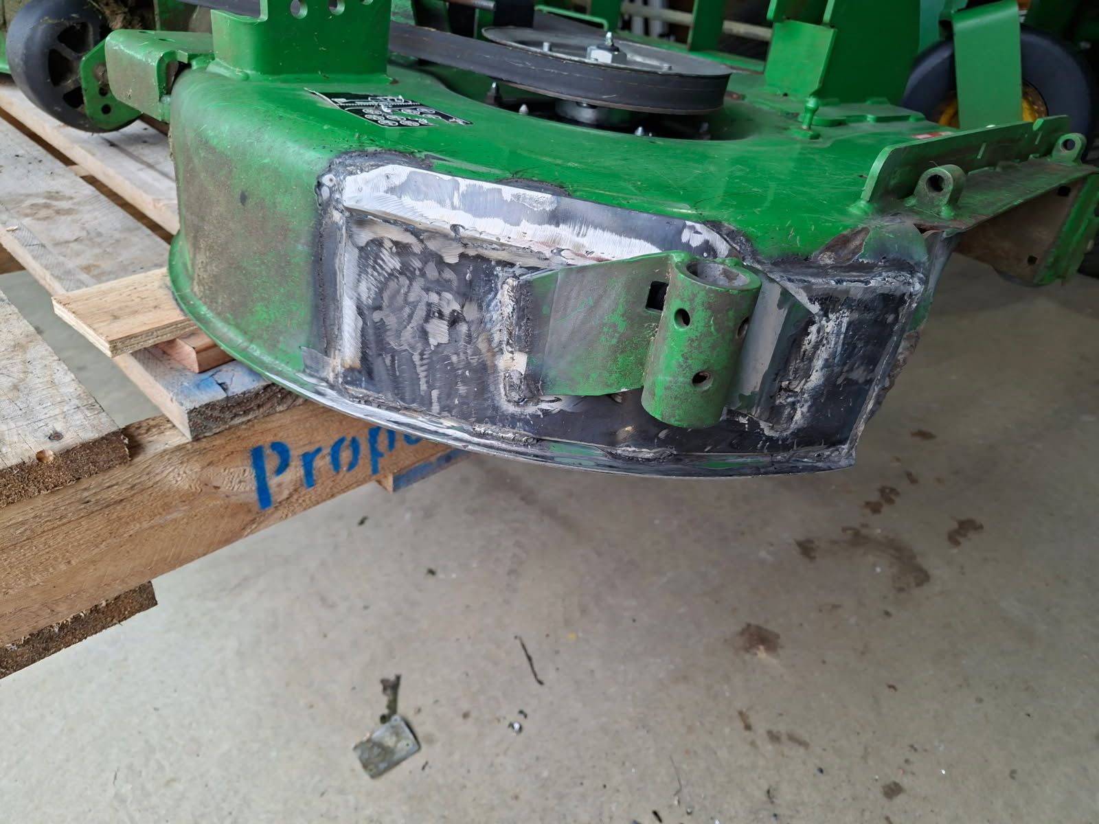 The same ride-on mower cutting deck after repair, with new steel plate welded into the front section and the bracket re-fitted