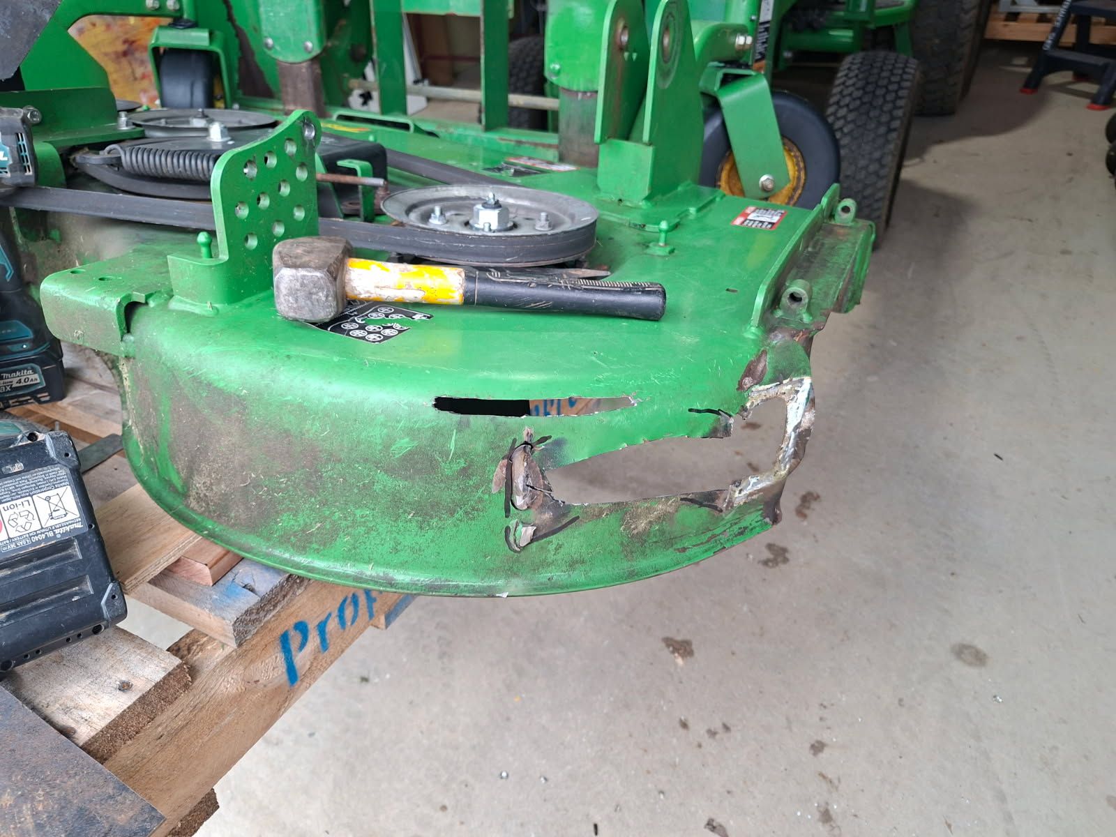 Ride-on mower cutting deck with the front section torn open and holed, before repair