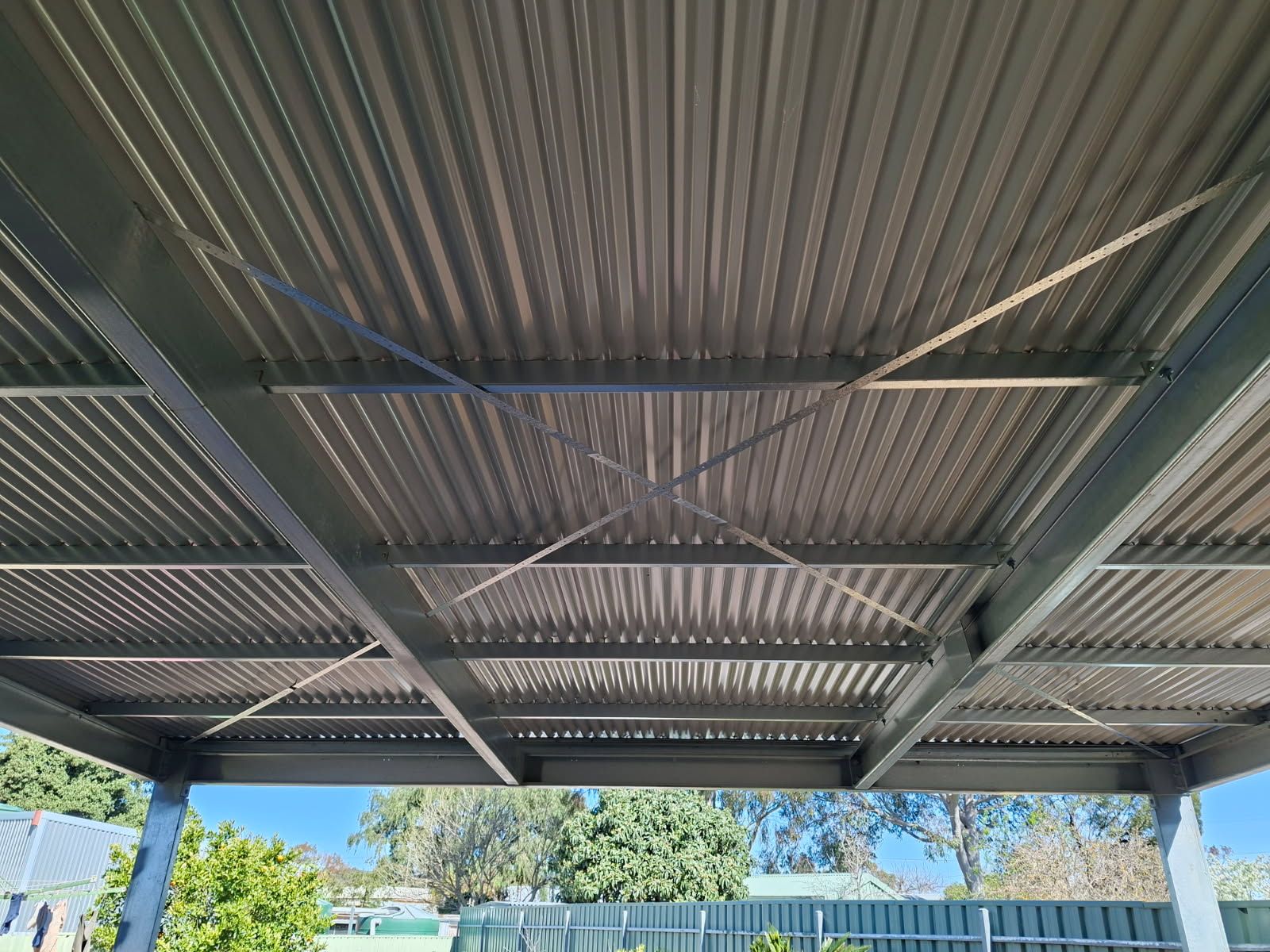 Looking up at the underside of a new steel pergola in Tanunda: steel beams, purlins and cross-bracing on steel posts under a corrugated roof
